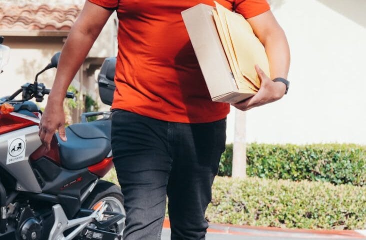 smiling man in red crew neck t shirt carrying a package for delivery