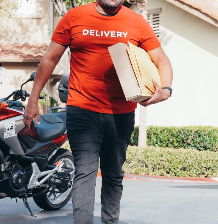 smiling man in red crew neck t shirt carrying a package for delivery